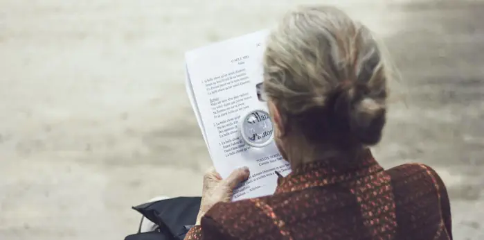 An aged woman using a magnifying glass to view a document about AustralianSuper fixed cover option