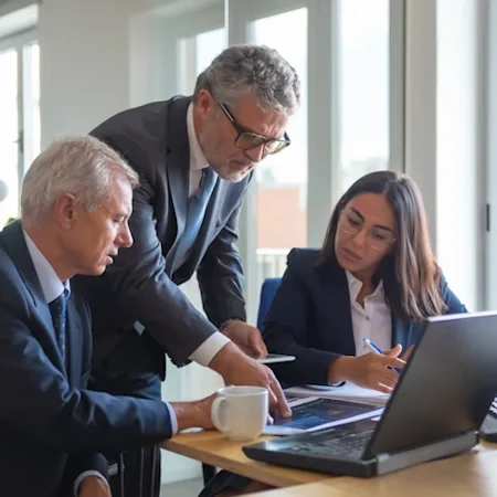 Three critical illness lawyers looking at a laptop and discussing a trauma insurance claim