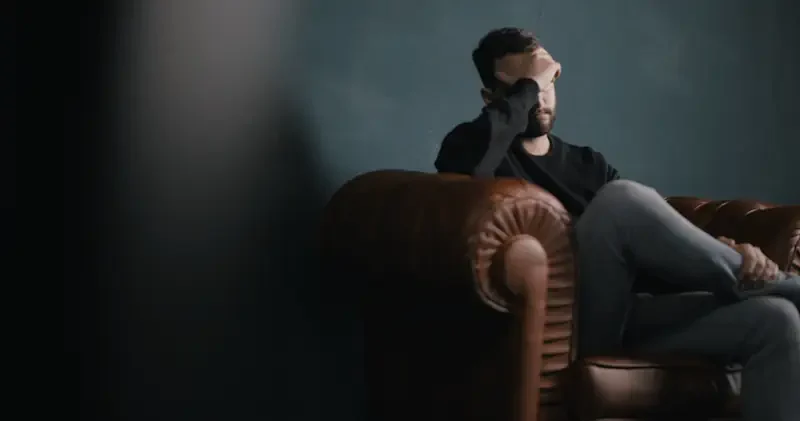 A depressed man suffering from post traumatic stress disorder sitting on a couch