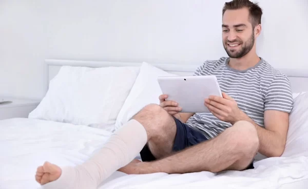 A man with broken leg on his bed viewing a tpd insurance policy on an ipad